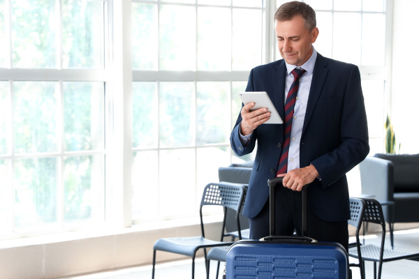 Señor de pie en el aeropuerto interactuando con su tablet